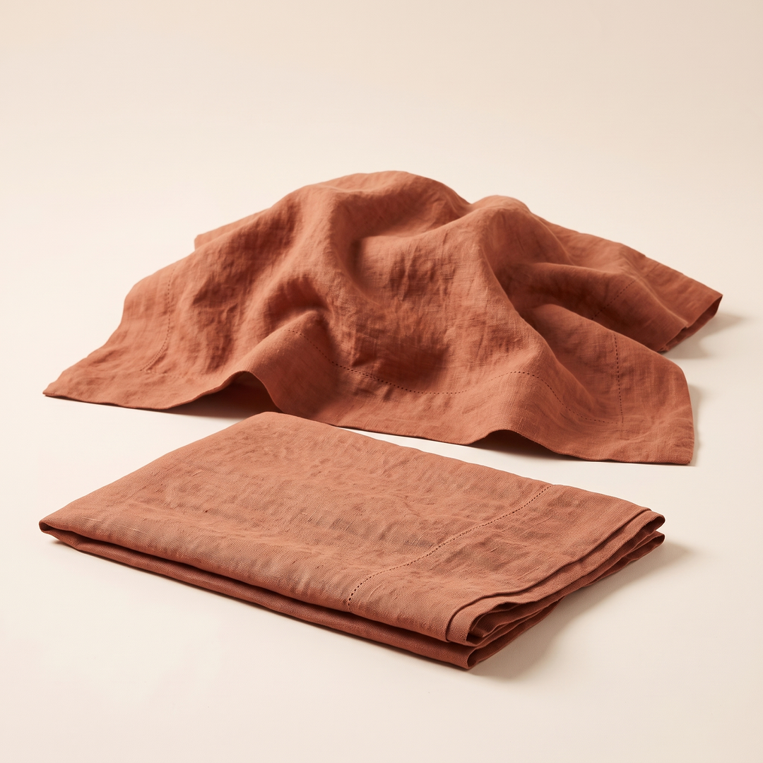 Linen Pillowcases – Set of 2 in Rust – one loosely rumpled and spread out behind a folded one