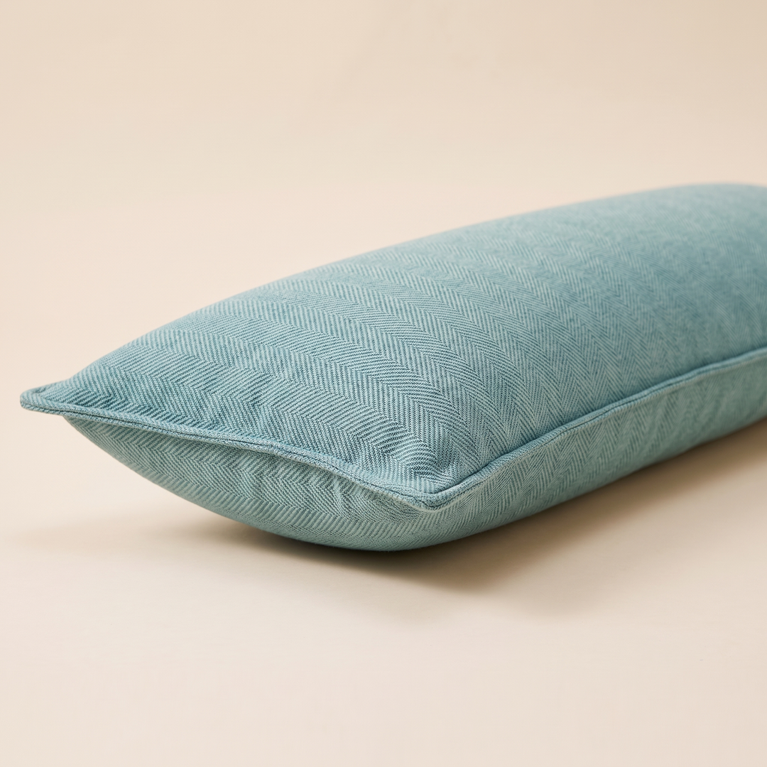 Long Lumbar Pillow Cover in Aqua – lying on its side at low angle on a plain peach surface