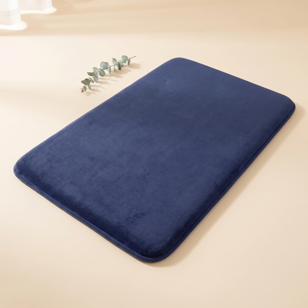 Non-Slip Memory Foam Bath Mat – Plush in Navy Blue – with a eucalyptus sprig beside it in soft sunlight