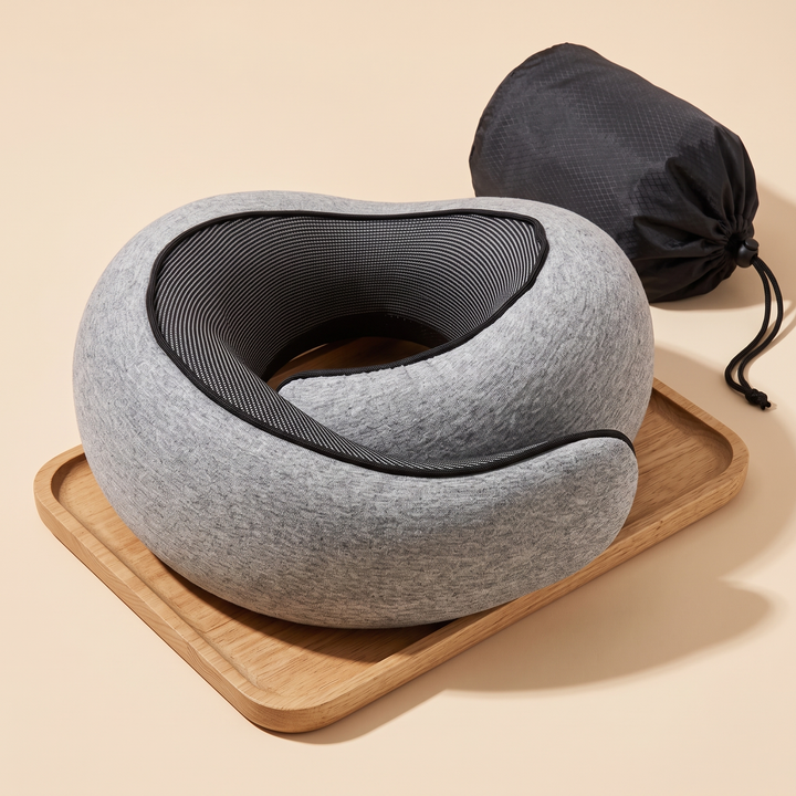 Memory Foam Neck Pillow for Travel in Gray – angled view resting on a wooden tray beside a drawstring bag