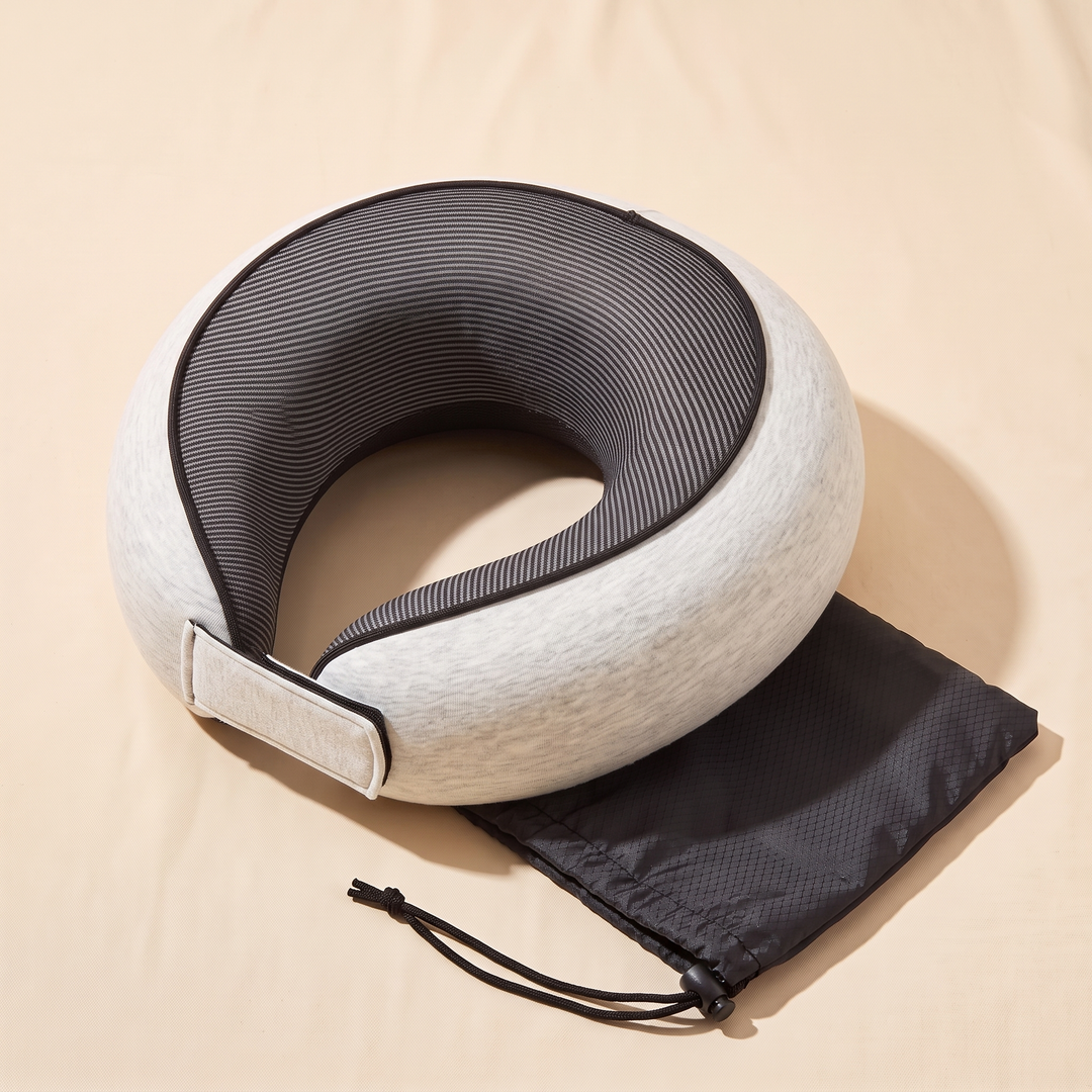 Memory Foam Neck Pillow for Travel in Light Gray – overhead view lying flat, overlapping a black drawstring bag