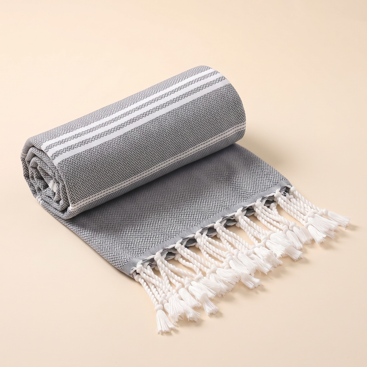 Oversized Beach Towel with Tassels in Charcoal – rolled up loosely with fringe spilling over the front edge