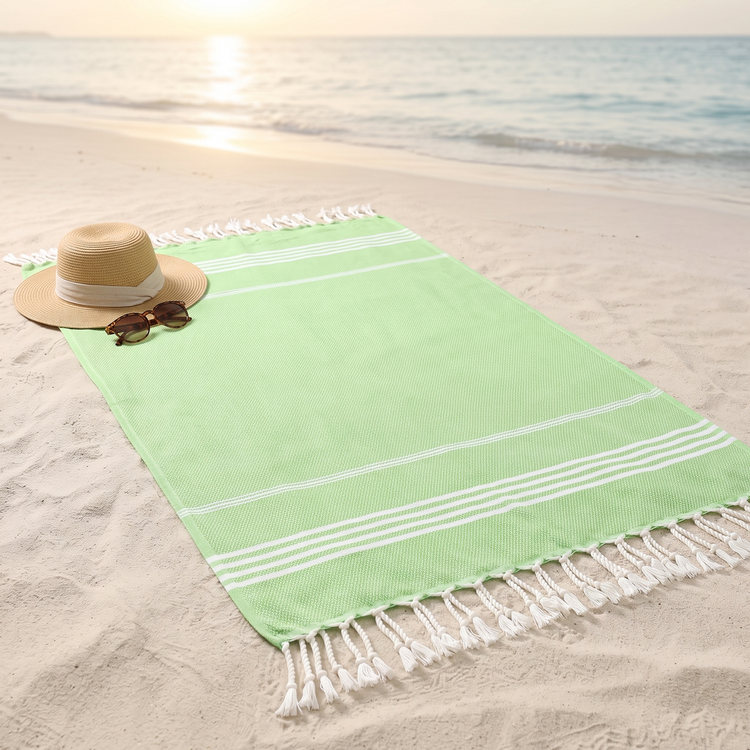 Oversized Beach Towel with Tassels in Light Green – spread on sandy beach beside a straw hat and sunglasses