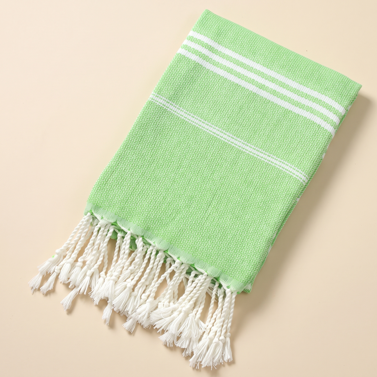 Oversized Beach Towel with Tassels in Light Green – folded flat on a plain peach background, tassels at the bottom
