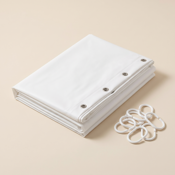 Shower Curtain Liner – Clear PEVA with Magnets in White – folded neatly on a plain beige surface beside plastic rings
