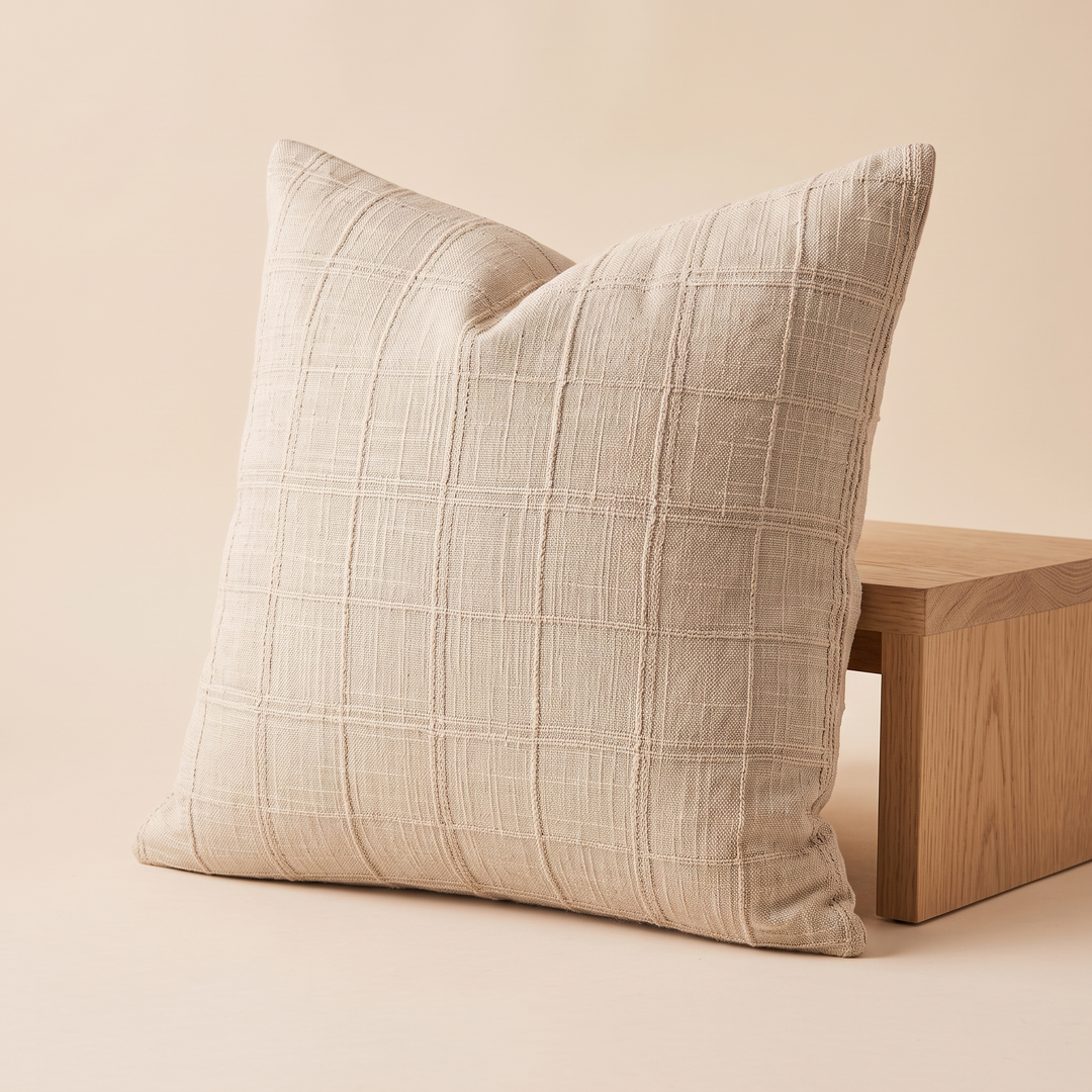 Plaid Pillow Cover – Textured Grid Check in Cream – standing upright against a wooden bench on a peach backdrop