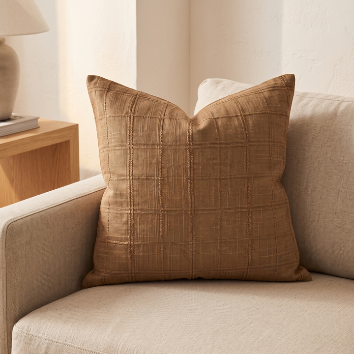 Plaid Pillow Cover – Textured Grid Check in Brown – propped in the corner of a beige sofa beside a wooden side table