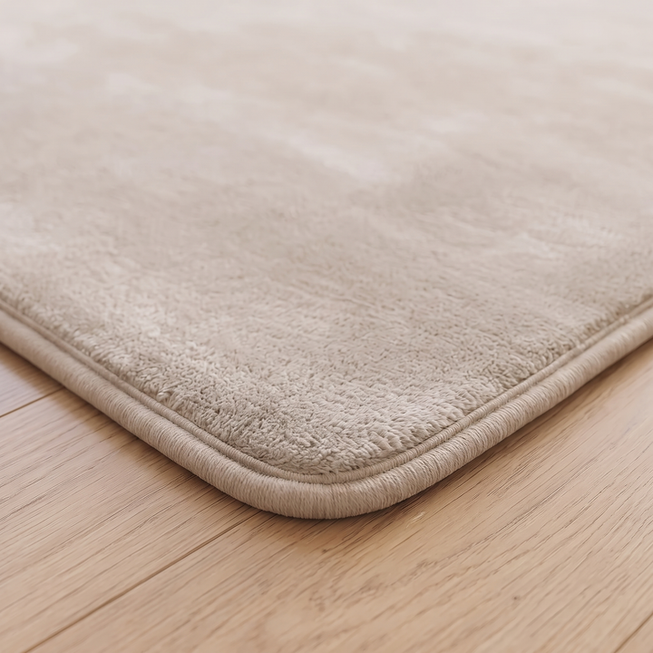 Plush Area Rug in Beige – close-up of a rounded corner and bound edge on wood flooring