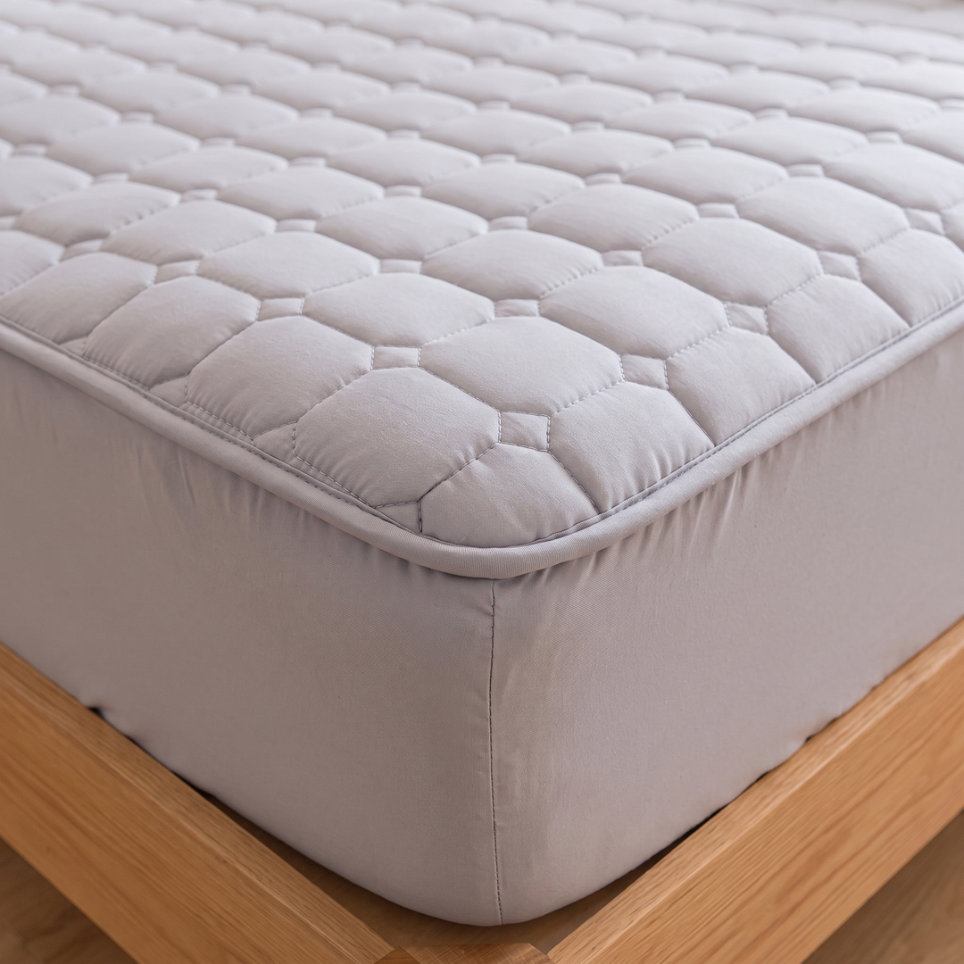 Quilted Mattress Protector – Cotton Top, Fitted in Gray – close-up of a quilted corner fitted over a mattress on a wooden frame