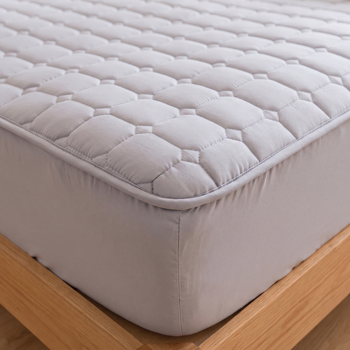 Quilted Mattress Protector – Cotton Top, Fitted in Gray – close-up of a quilted corner fitted over a mattress on a wooden frame