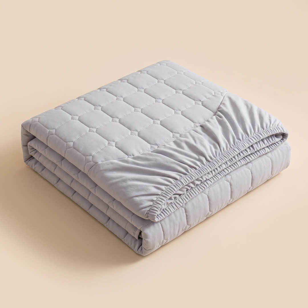 Quilted Mattress Protector – Cotton Top, Fitted in Gray – folded in a neat stack on a plain beige background