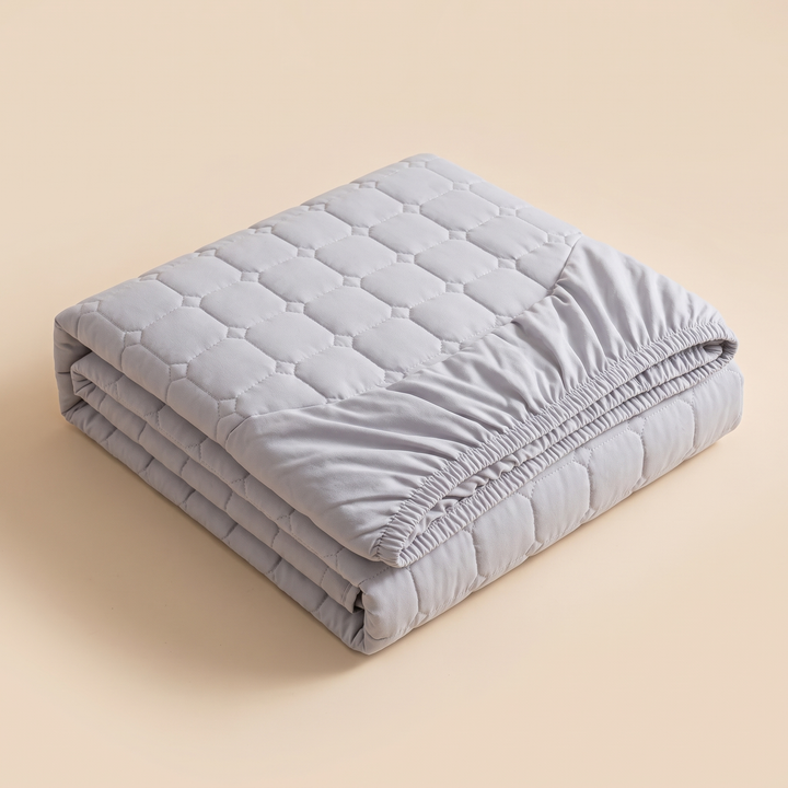 Quilted Mattress Protector – Cotton Top, Fitted in Gray – folded in a neat stack on a plain beige background