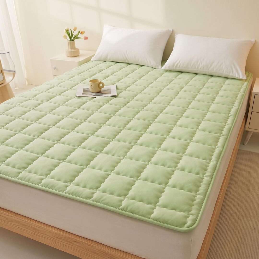 Quilted Mattress Pad in Light Green – angled view on bed with a mug and tulips nearby
