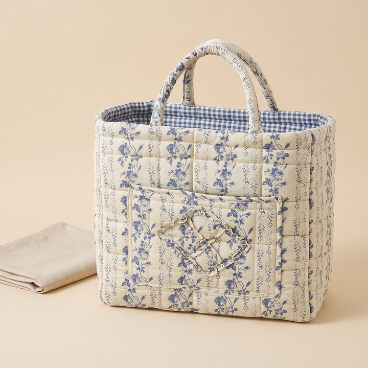 Quilted Fabric Storage Basket with Handles in Blue – Floral Vine – beside a folded linen cloth on a plain backdrop