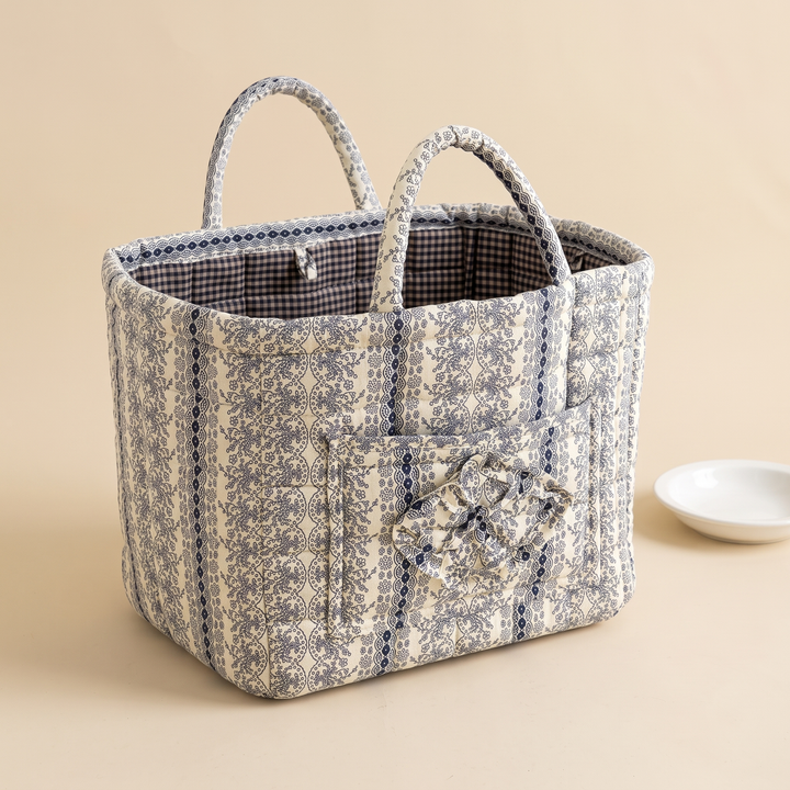Quilted Fabric Storage Basket with Handles in Navy – Floral Stripe – beside a small white dish on a tan tabletop