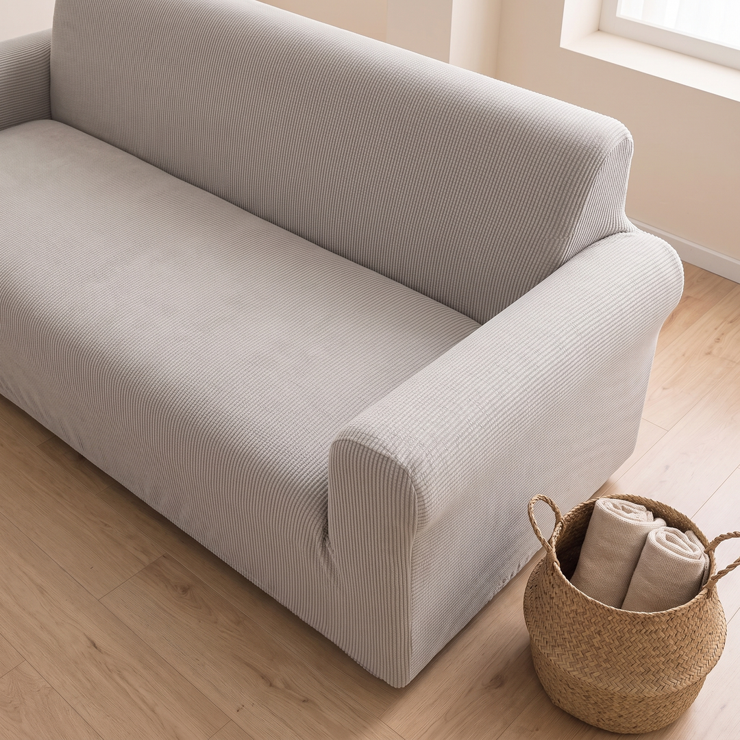Ribbed Stretch Couch Cover in Light Gray – overhead angle beside a woven basket on a wood floor