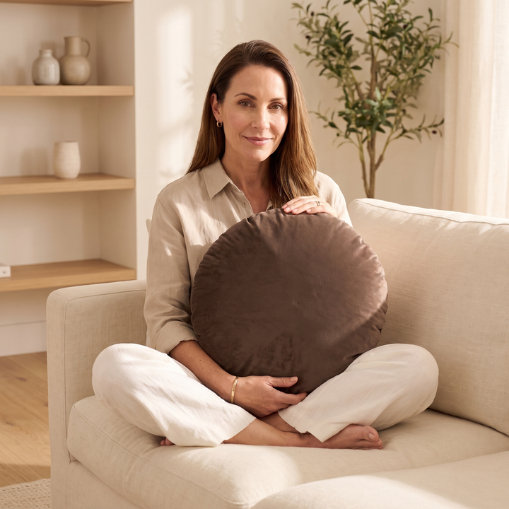 Round Velvet Pillow Cover in Chocolate Brown – held on lap by a woman sitting cross-legged
