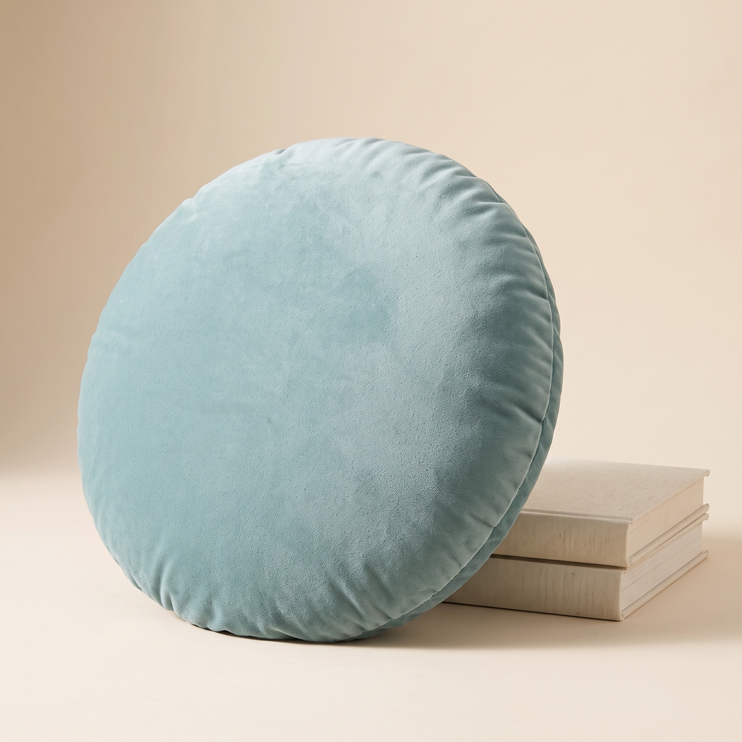 Round Velvet Pillow Cover in Aqua – leaning against a stack of cream books on a beige surface