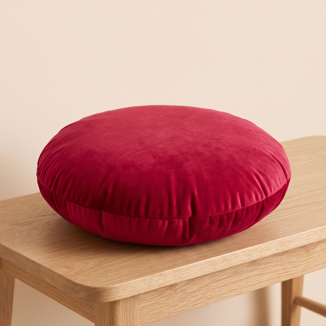 Round Velvet Pillow Cover in Crimson Red – lying flat on a light wood bench against a peach wall