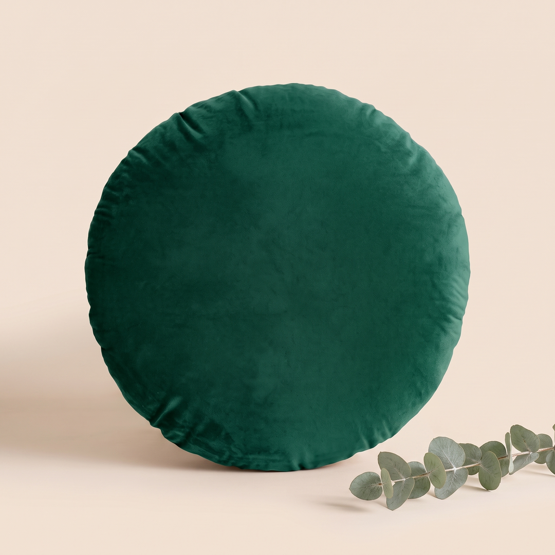 Round Velvet Pillow Cover in Emerald Green – upright with a eucalyptus sprig resting in the lower corner