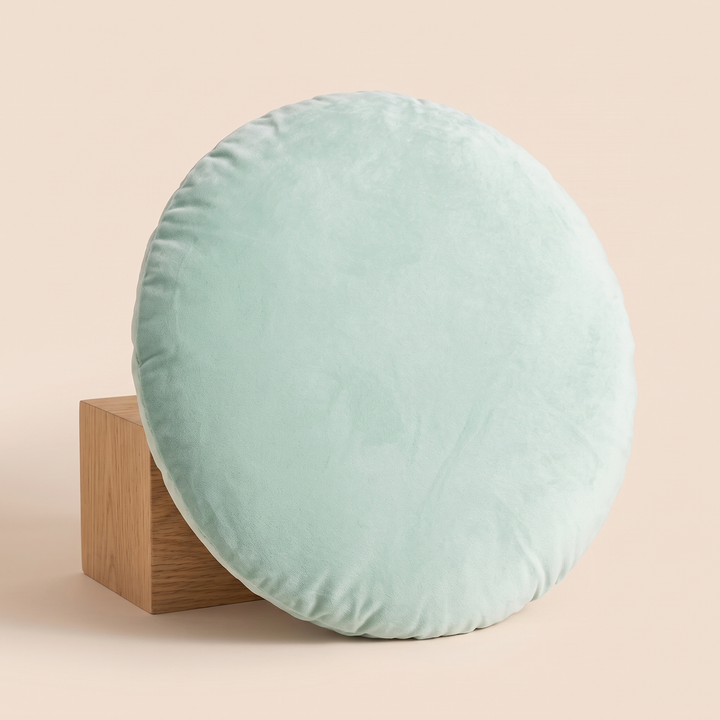 Round Velvet Pillow Cover in Mint Green – leaning against a wooden block on a peach backdrop