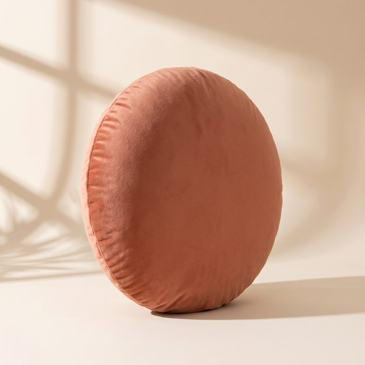 Round Velvet Pillow Cover in Rust – upright in warm sunlight with window shadows across the wall