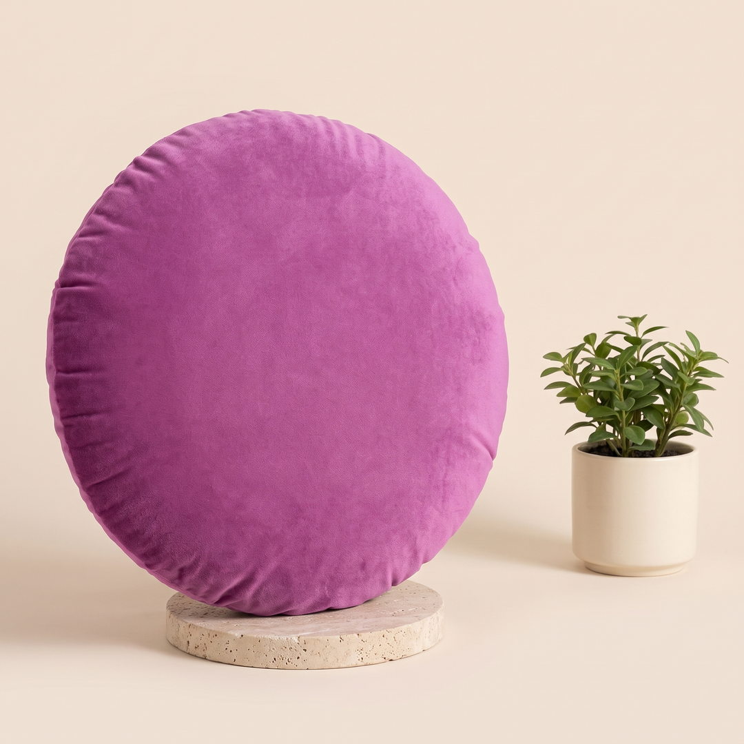 Round Velvet Pillow Cover in Violet – standing on a travertine disc beside a potted green plant