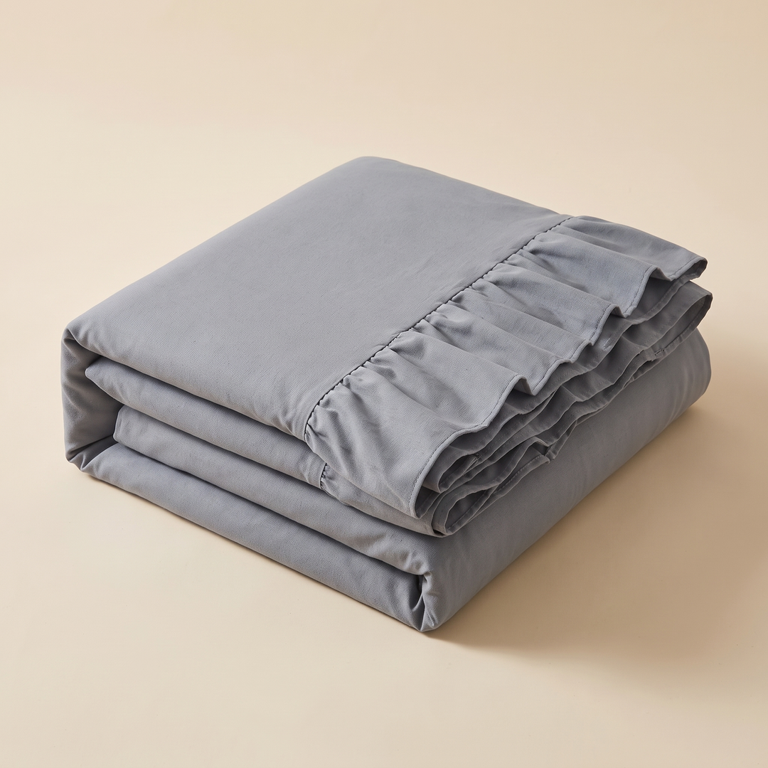 Ruffled Couch Cover in Gray – neatly folded stack with ruffled edge on plain beige background