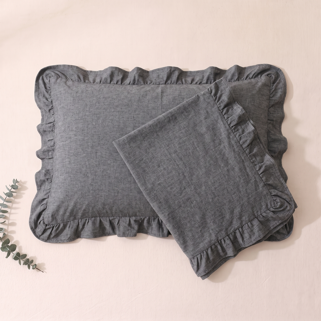 Cotton Pillowcases – Ruffled Plaid, Set of 2 in Dark Gray – one case turned over another on blush sheet, eucalyptus sprig left
