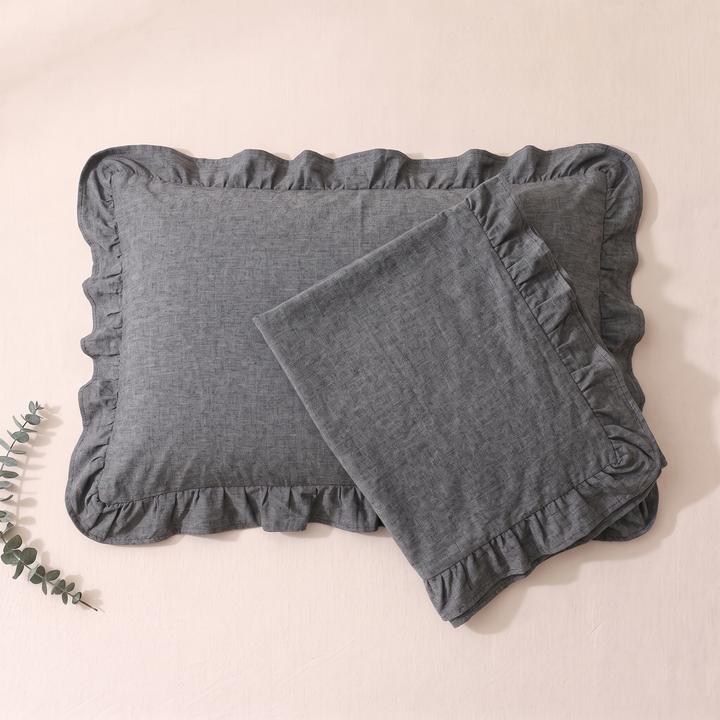 Cotton Pillowcases – Ruffled Plaid, Set of 2 in Dark Gray – one case turned over another on blush sheet, eucalyptus sprig left