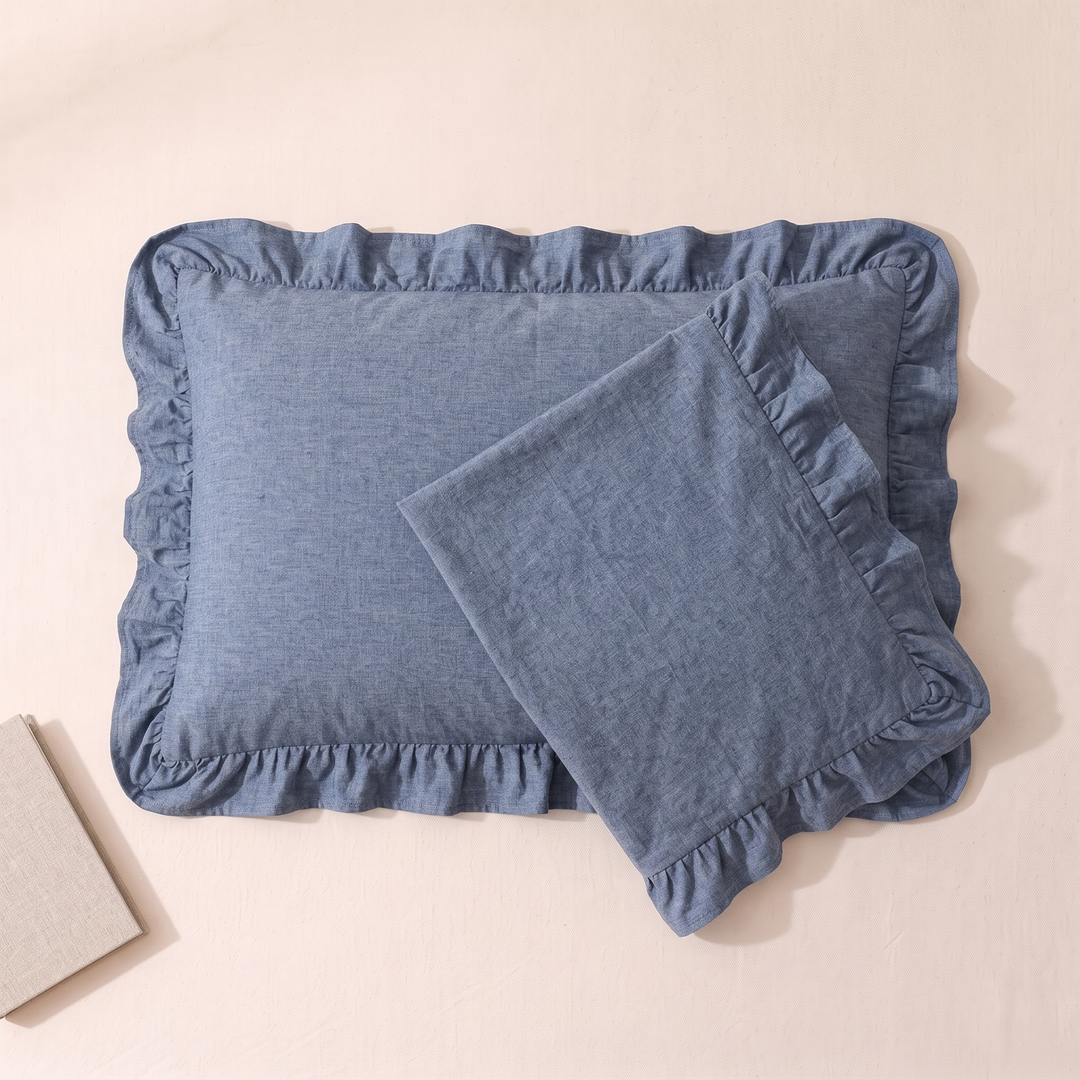 Cotton Pillowcases – Ruffled Plaid, Set of 2 in Denim Blue – overlapping pair on pale peach surface, book corner lower left