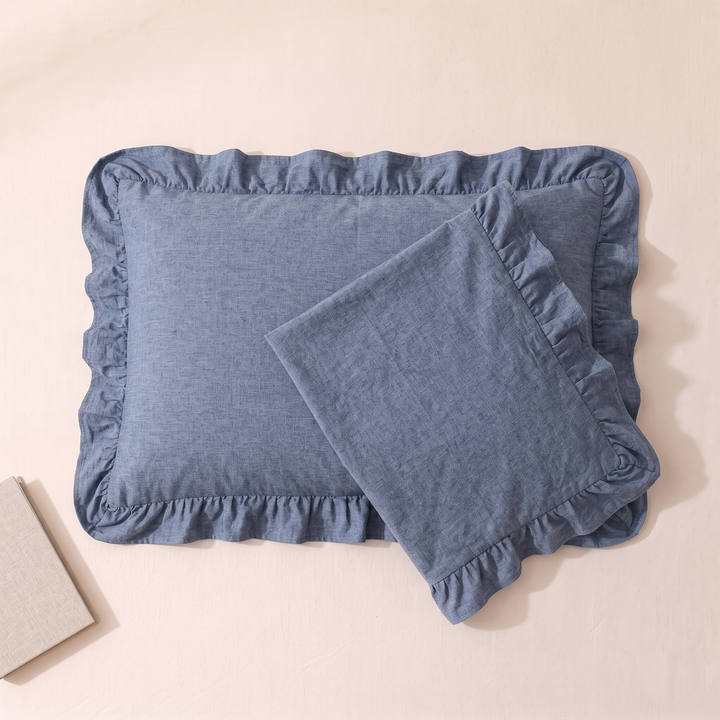 Cotton Pillowcases – Ruffled Plaid, Set of 2 in Denim Blue – overlapping pair on pale peach surface, book corner lower left