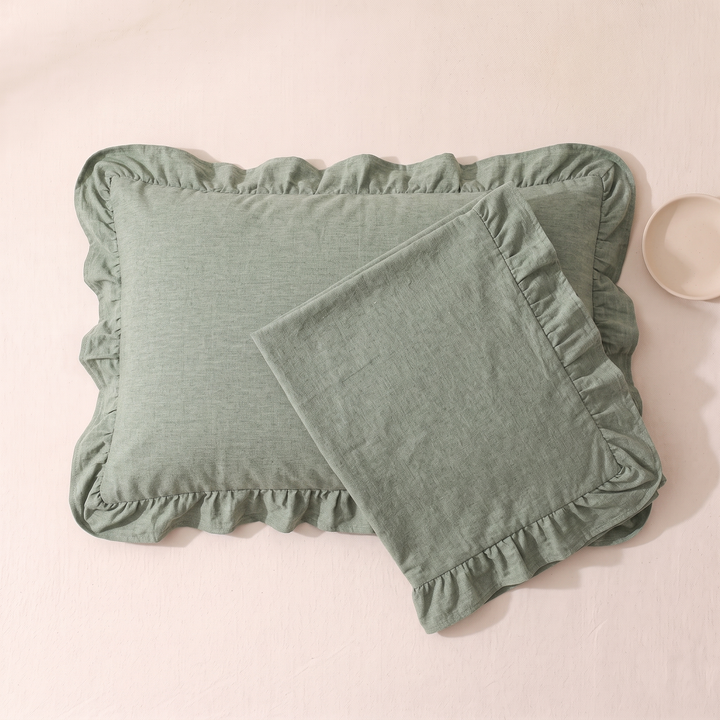 Cotton Pillowcases – Ruffled Plaid, Set of 2 in Sage – overlapping pair on pale pink surface beside a small bowl