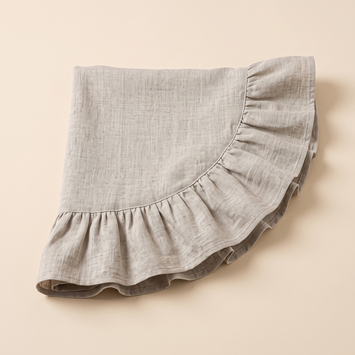 Ruffled Round Tablecloth in Beige – folded flat on a plain peach background, ruffled edge curving across the front