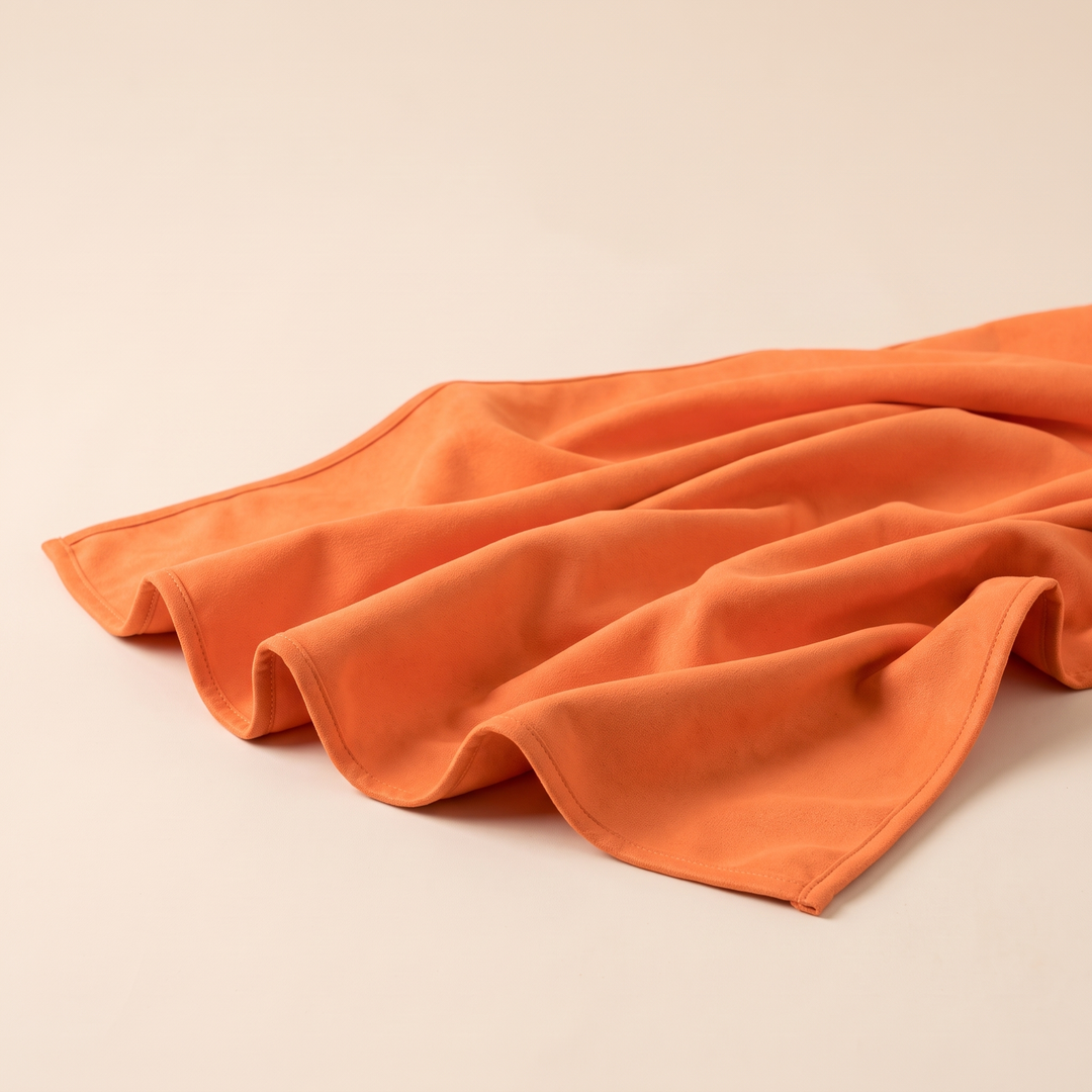 Sand-Free Beach Towel – Quick-Dry in Bright Orange – spread out in loose ripples on a plain cream surface