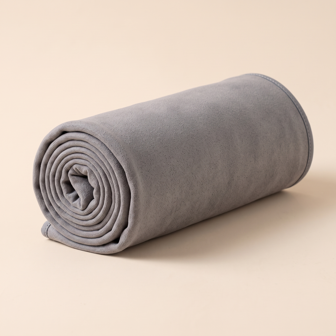 Sand-Free Beach Towel – Quick-Dry in Gray – rolled up into a tight cylinder on a plain peach background
