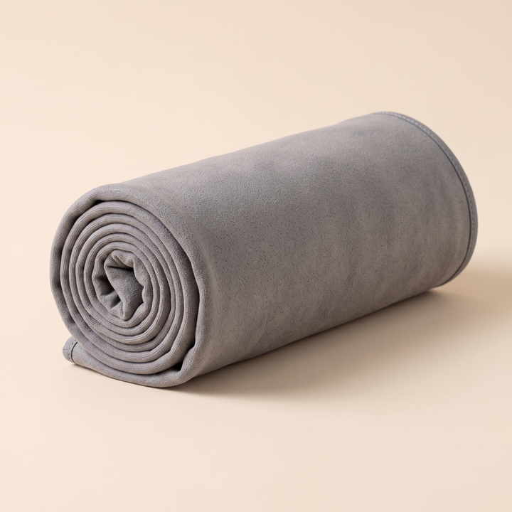 Sand-Free Beach Towel – Quick-Dry in Gray – rolled up into a tight cylinder on a plain peach background