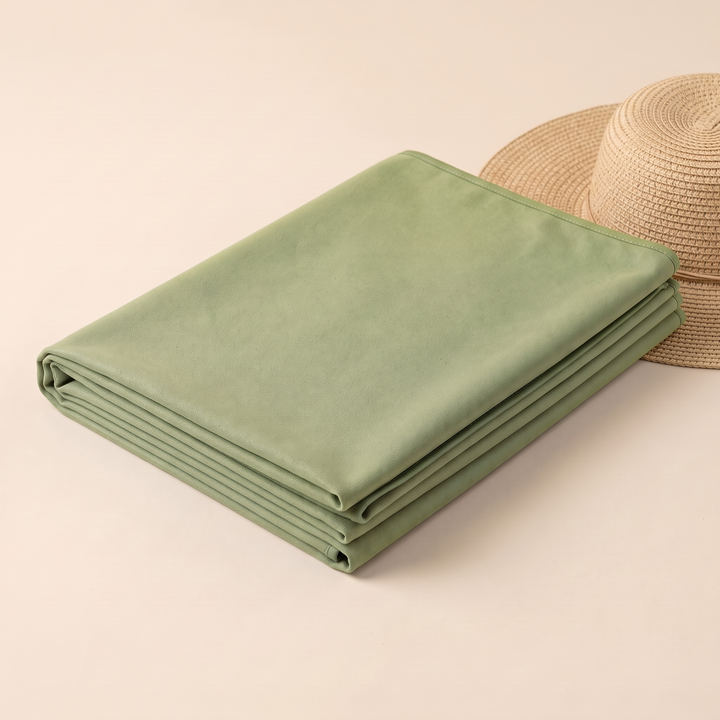 Sand-Free Beach Towel – Quick-Dry in Moss Green – folded stack resting against a woven straw hat