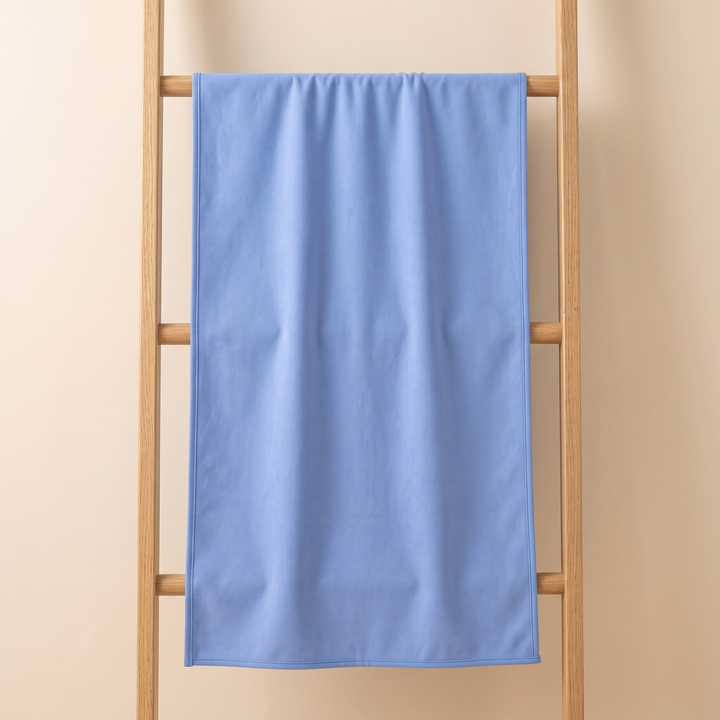 Sand-Free Beach Towel – Quick-Dry in Periwinkle Blue – hanging over a wooden ladder rung against a beige wall