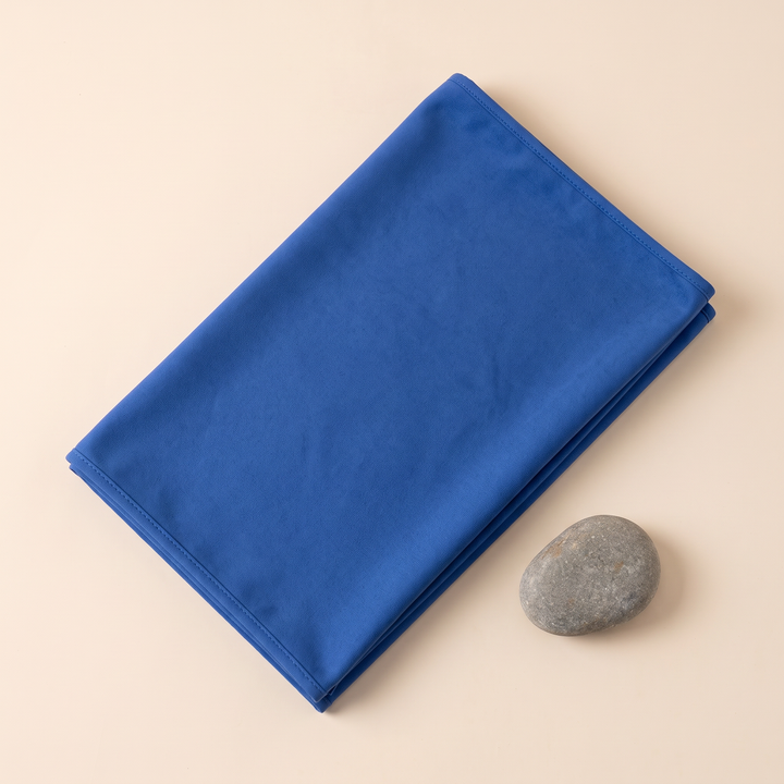 Sand-Free Beach Towel – Quick-Dry in Royal Blue – folded rectangle with a smooth gray pebble beside it, overhead