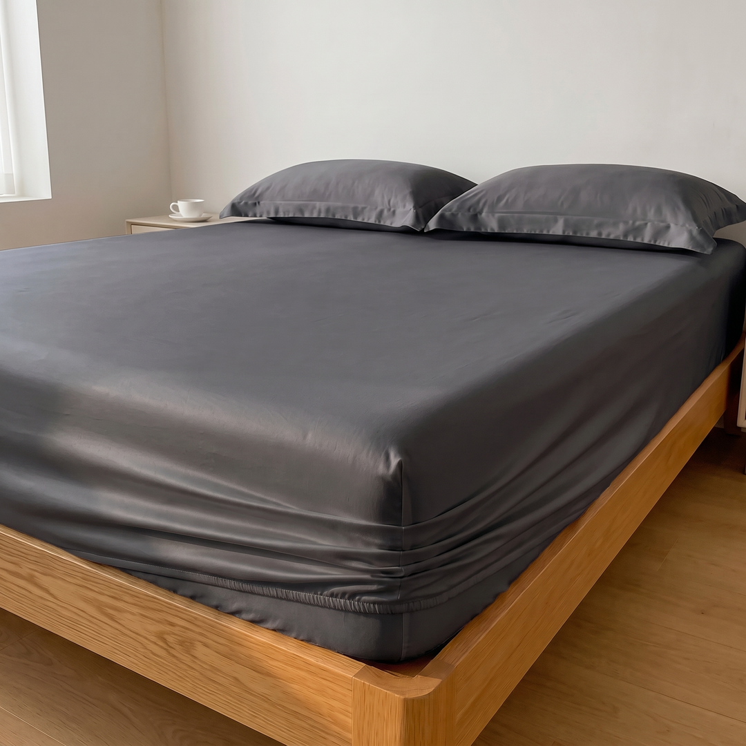 Sateen Fitted Sheet Set with 2 Pillowcases in Dark Gray – corner view with a teacup on the bedside table