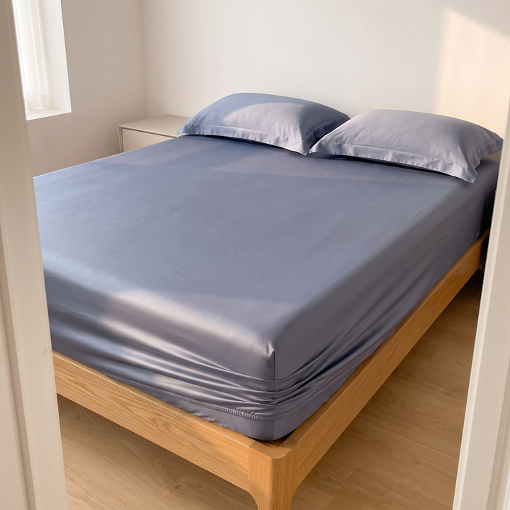 Sateen Fitted Sheet Set with 2 Pillowcases in Dusty Blue – seen through a bedroom doorway with a white nightstand beyond