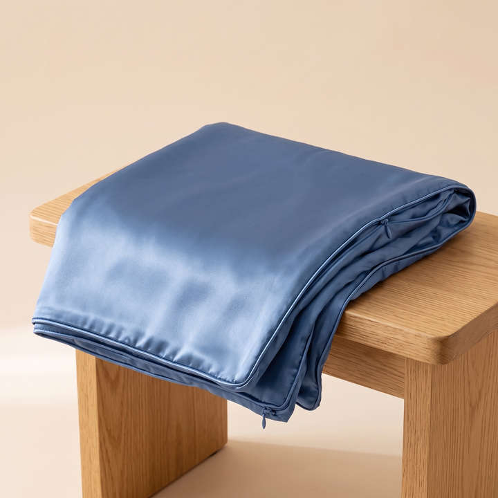 Satin Pillowcase for Contour Pillows in Blue – folded with one side hanging over a wooden stool edge