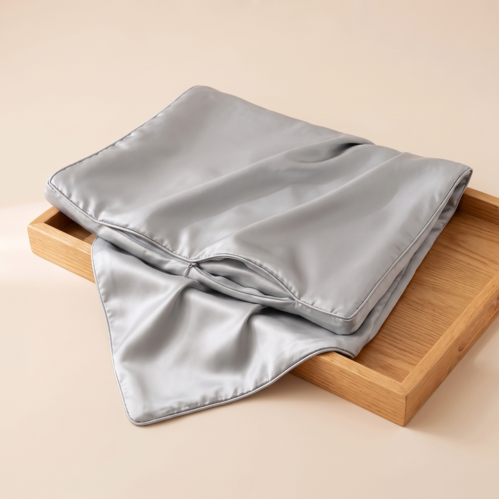 Satin Pillowcase for Contour Pillows in Gray – folded and resting partly on a wooden tray, with the zipper opening visible
