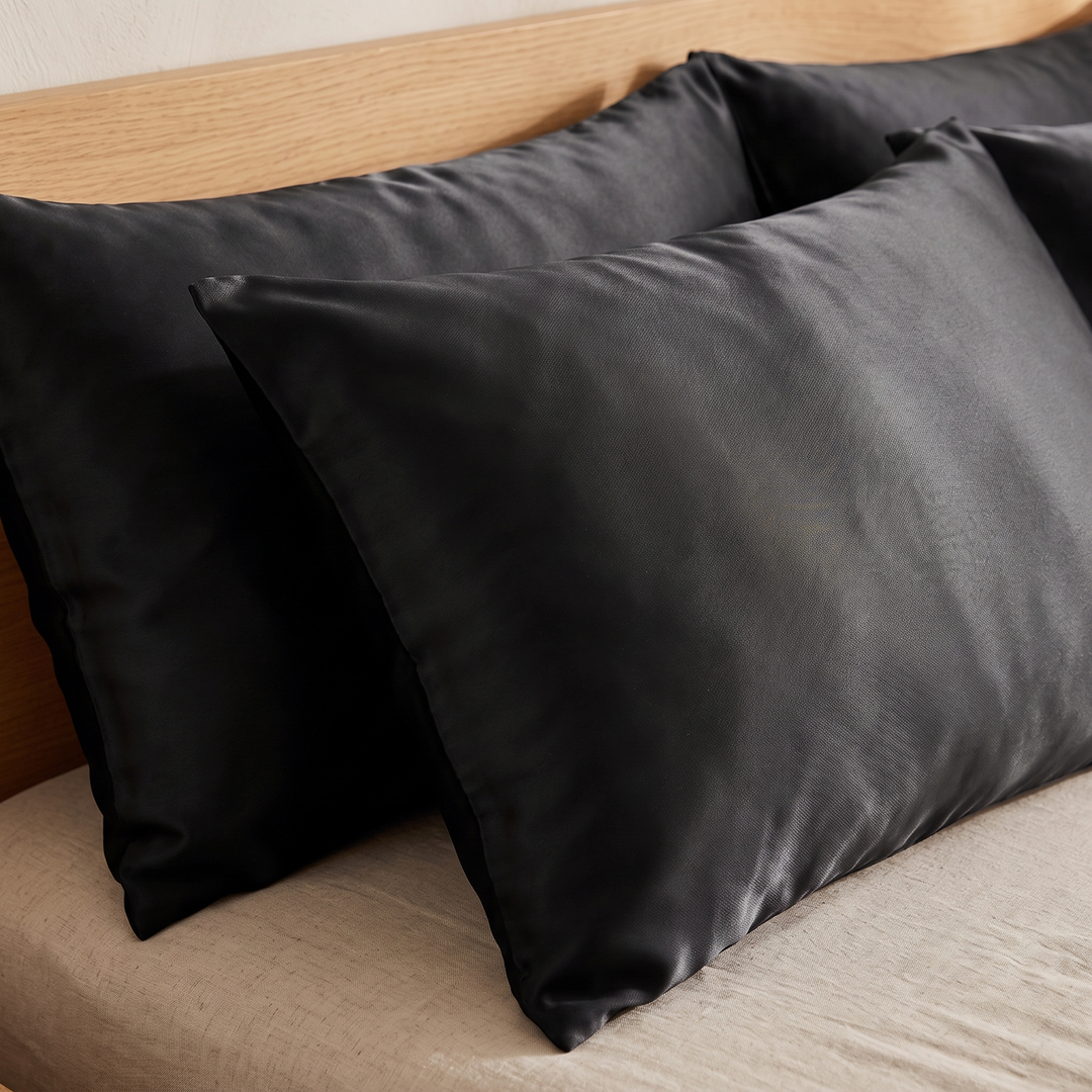 Black satin pillowcases on a made bed