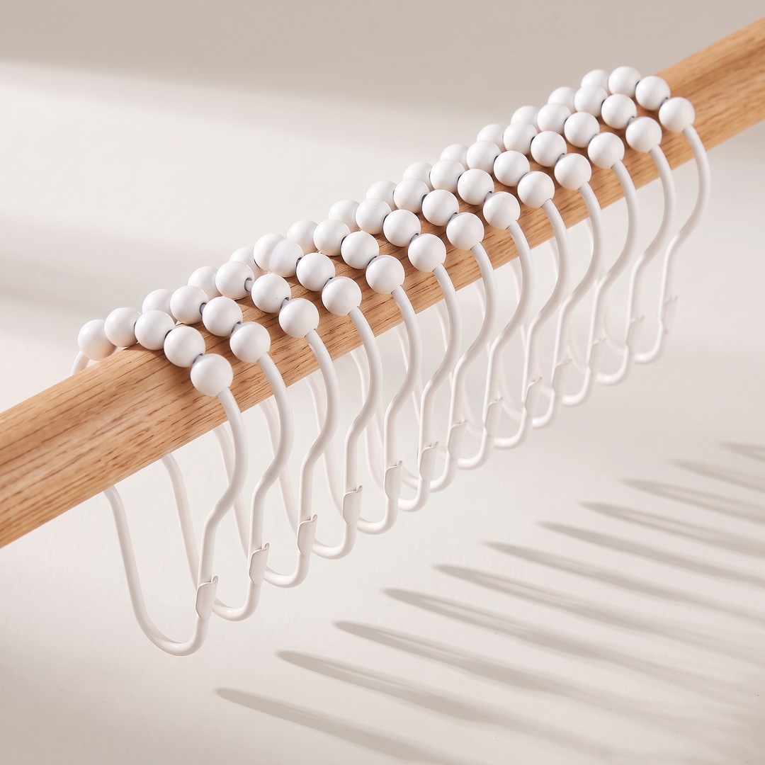 Shower Curtain Hooks – Set of 12, Roller Ball in White – lined up along a wooden pole, casting shadows on a plain surface