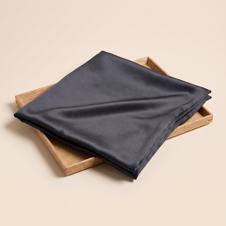 Silk Pillowcase – 19 Momme in Dark Gray – folded on a shallow wooden tray, seen from a three-quarter angle
