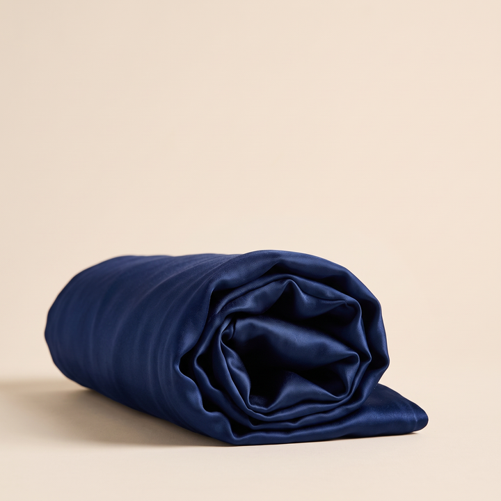Silk Pillowcase – 19 Momme in Midnight Blue – tightly rolled into a spiral, seen from the end on a cream background