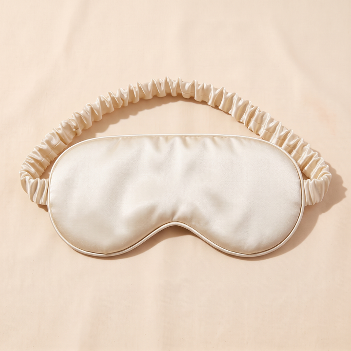 Silk Sleep Mask in Cream – centered overhead view, band arched with soft shadows beneath