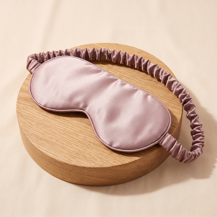 Silk Sleep Mask in Dusty Pink – draped over a round wooden block, strap hanging down